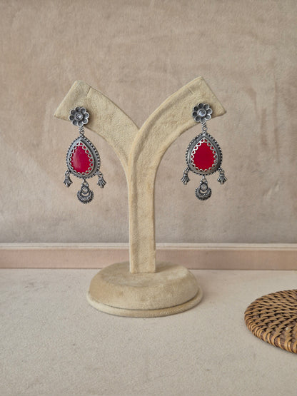 Pair of Kunti silver oxidized tear-drop earrings with a central red stone and small hanging charms by naitri.in