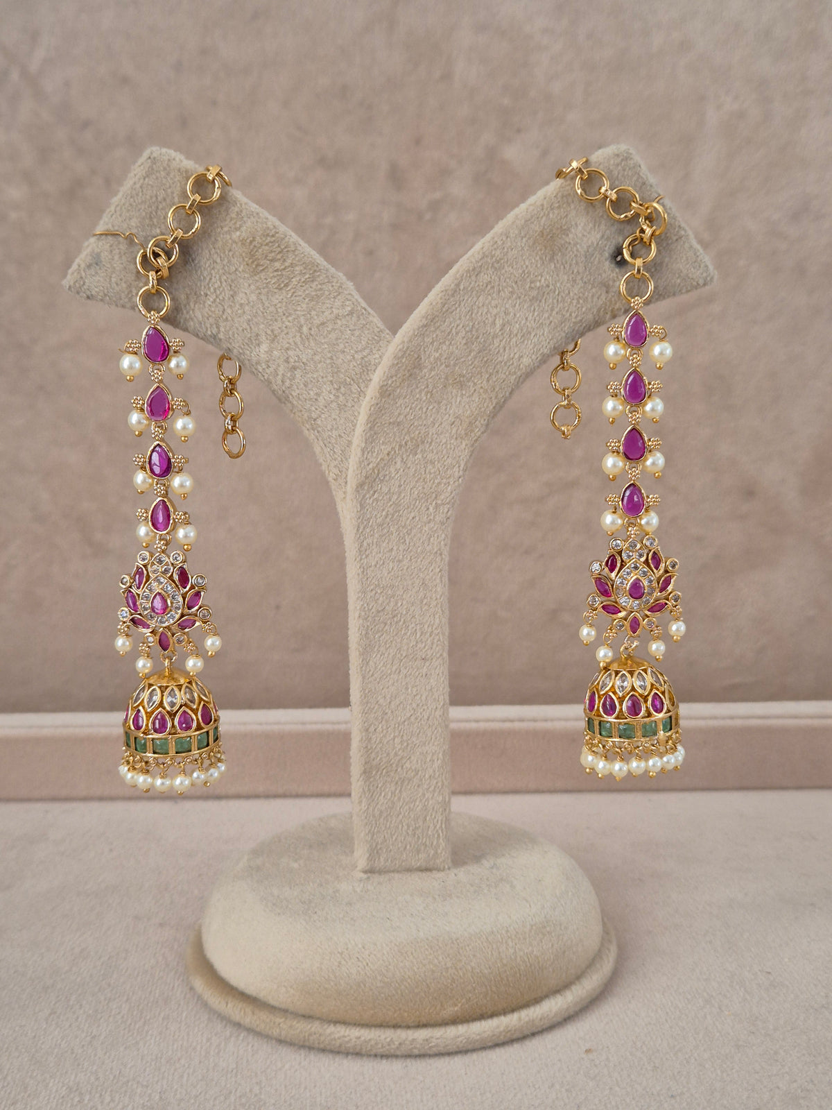 Pair of ornate gold-toned long dangle jhumka earrings featuring purple stone stud motifs, vertical strands of white pearls, and bell-shaped jhumkas with green enamel accents by naitri.in