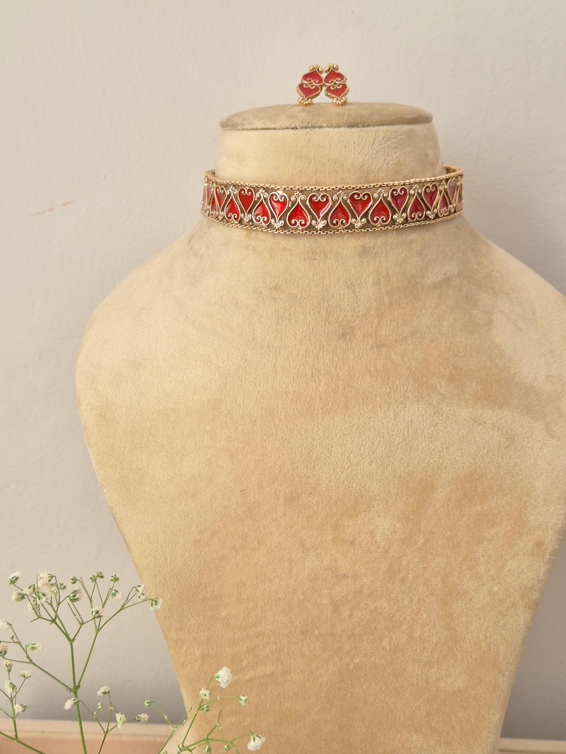 An elegant gold-plated choker necklace featuring a repeating pattern of red enamel heart-shaped motifs by naitri.in