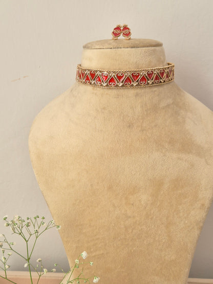An elegant gold-plated choker necklace featuring a repeating pattern of red enamel heart-shaped motifs by naitri.in