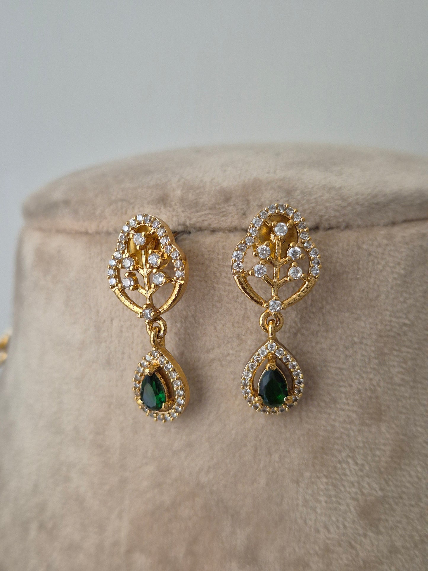 Golden leaf shaped earrings with green gemstones and white stones attached beautifully by naitri.in