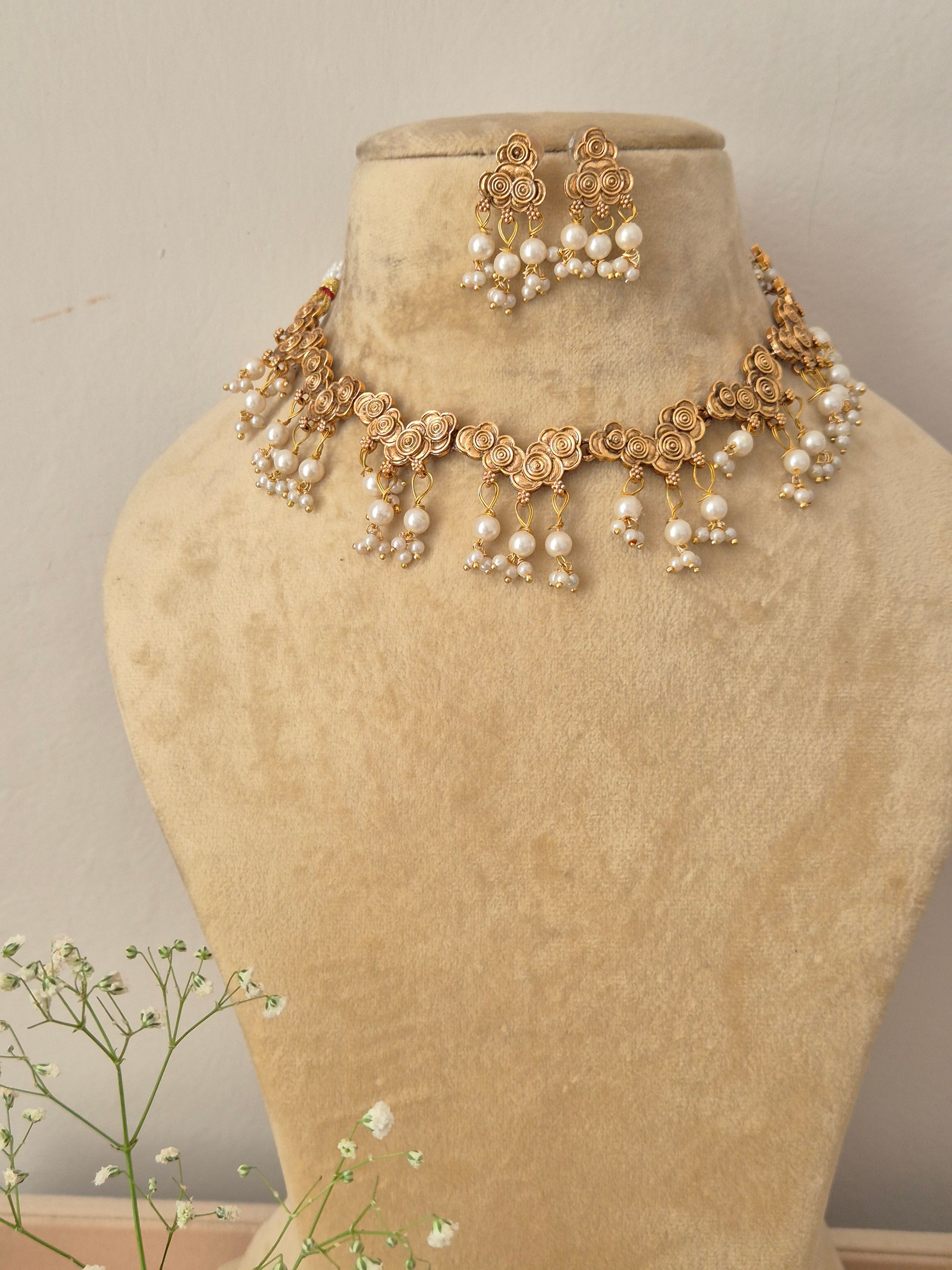 A gold-plated choker necklace featuring intricate floral metalwork motifs and hanging pearl drop clusters by naitri.in