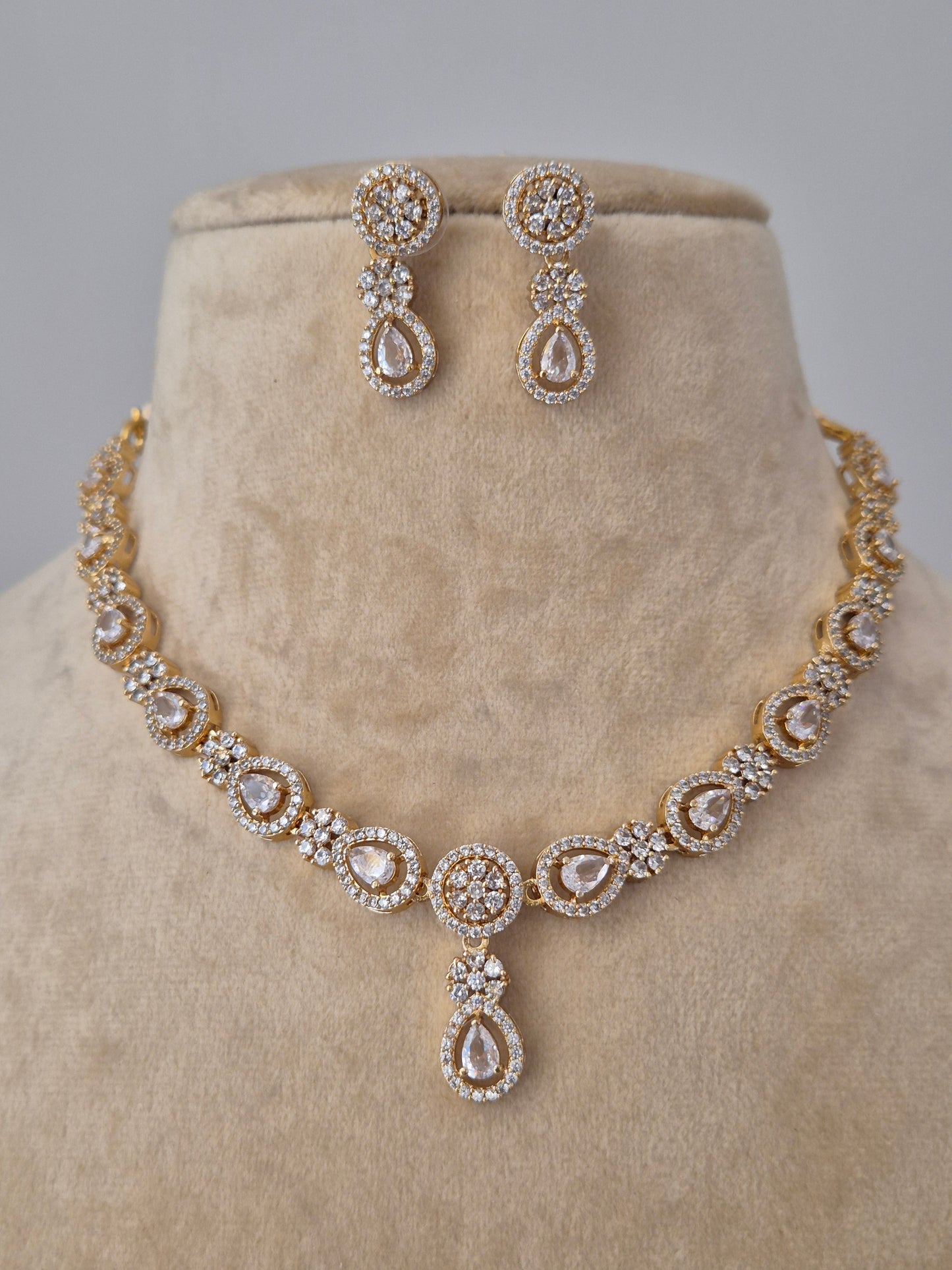 Pair of handcrafted golden necklace and  drop earrings featuring intricate stone-studded floral patterns by naitri.in