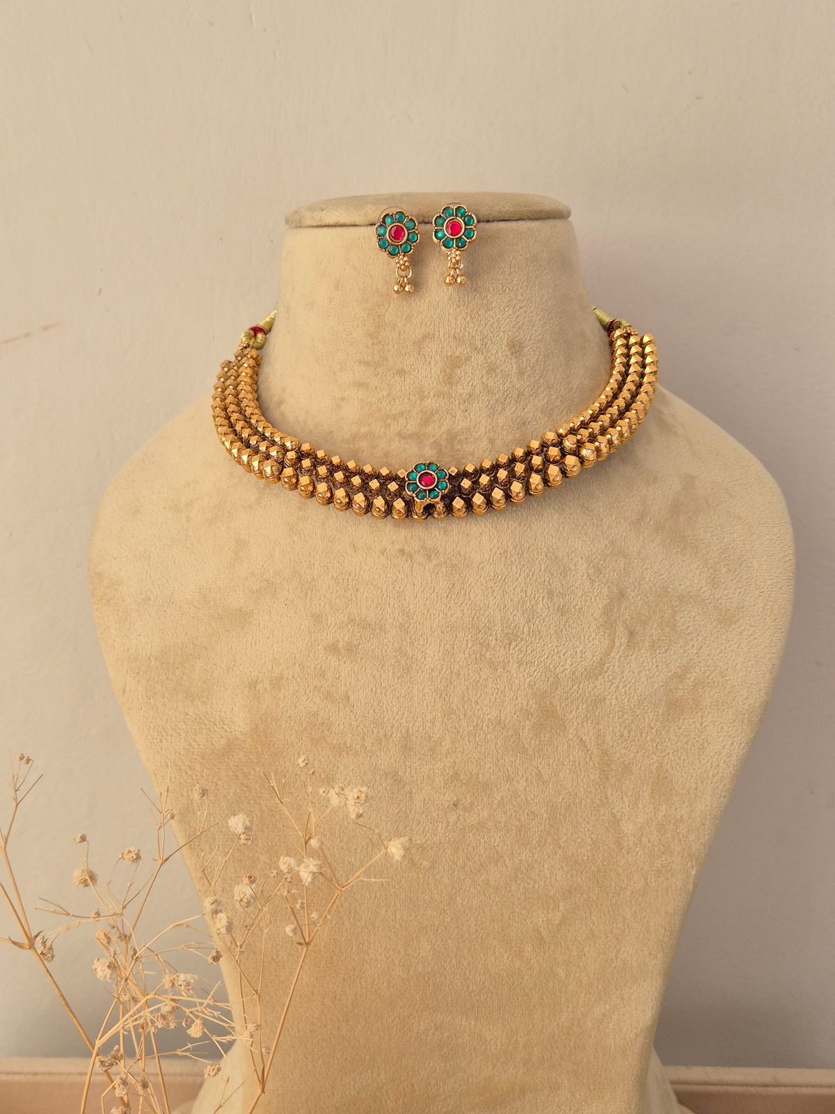 Madhuri Necklace Set featuring a multi-strand gold-toned beaded choker with a central flower motif set with green and pink stones, paired with matching stud earrings by Naitri.in