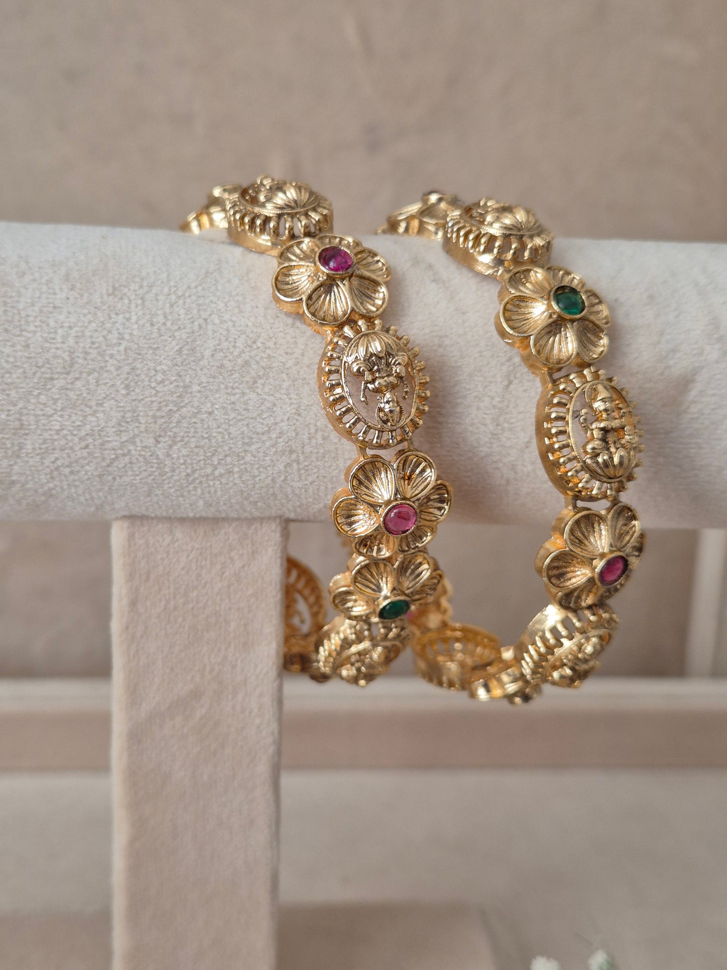 Two traditional gold-plated ethnic bangles with detailed floral motifs and inlaid red and green gemstones by naitri.in