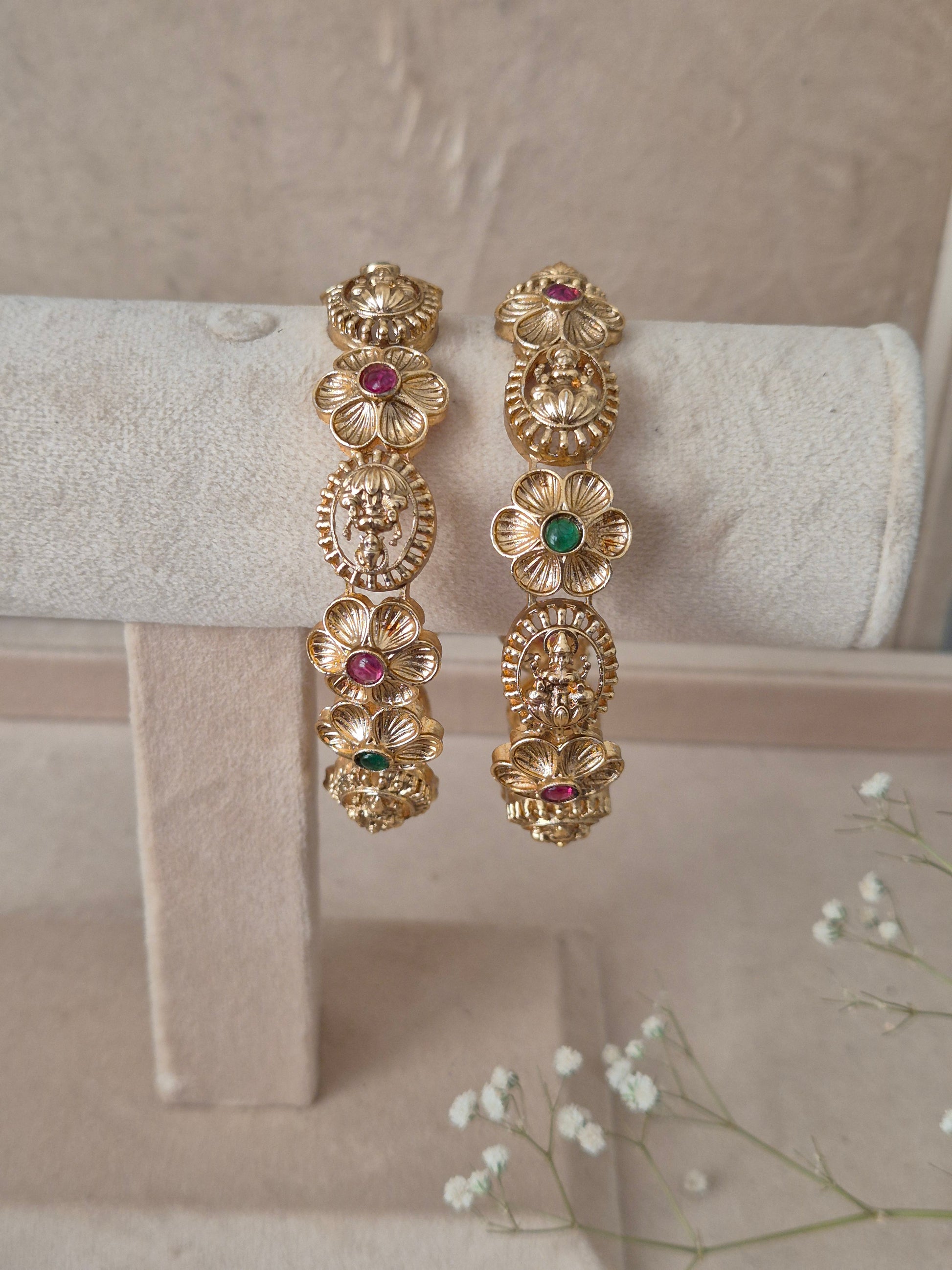 Pair of Naitri's Maitri gold bangles showcasing detailed antique craftsmanship, embedded with vibrant pinkish-red and green accent stones, by naitri.in