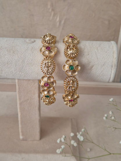 Pair of Naitri's Maitri gold bangles showcasing detailed antique craftsmanship, embedded with vibrant pinkish-red and green accent stones, by naitri.in