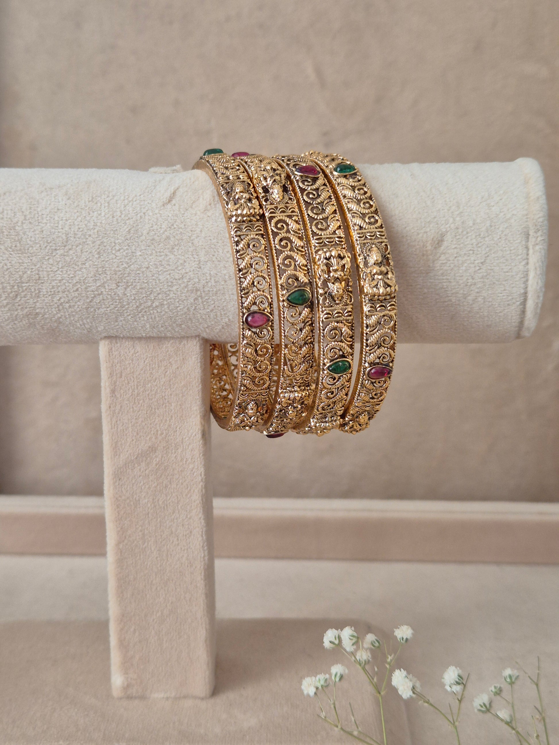 A stack of four Naitri Malati gold bangles showcasing detailed traditional craftsmanship, featuring vibrant pinkish-red floral motifs and green accent stones, by naitri.in