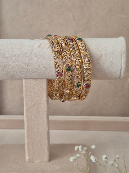 A stack of four Naitri Malati gold bangles showcasing detailed traditional craftsmanship, featuring vibrant pinkish-red floral motifs and green accent stones, by naitri.in