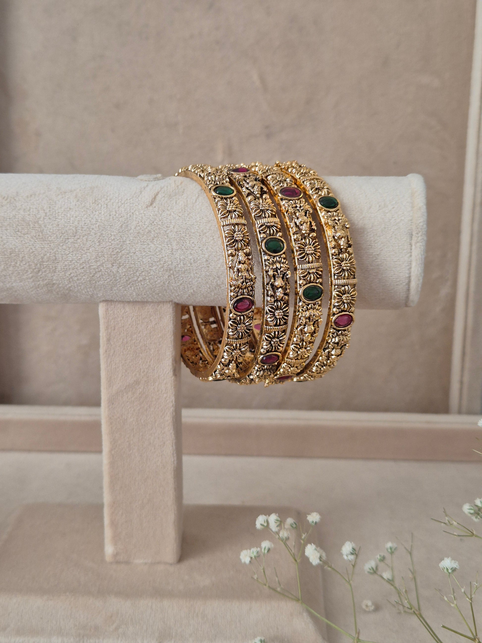 Set of four traditional gold-plated bridal bangles with red and green gemstones by naitri.in