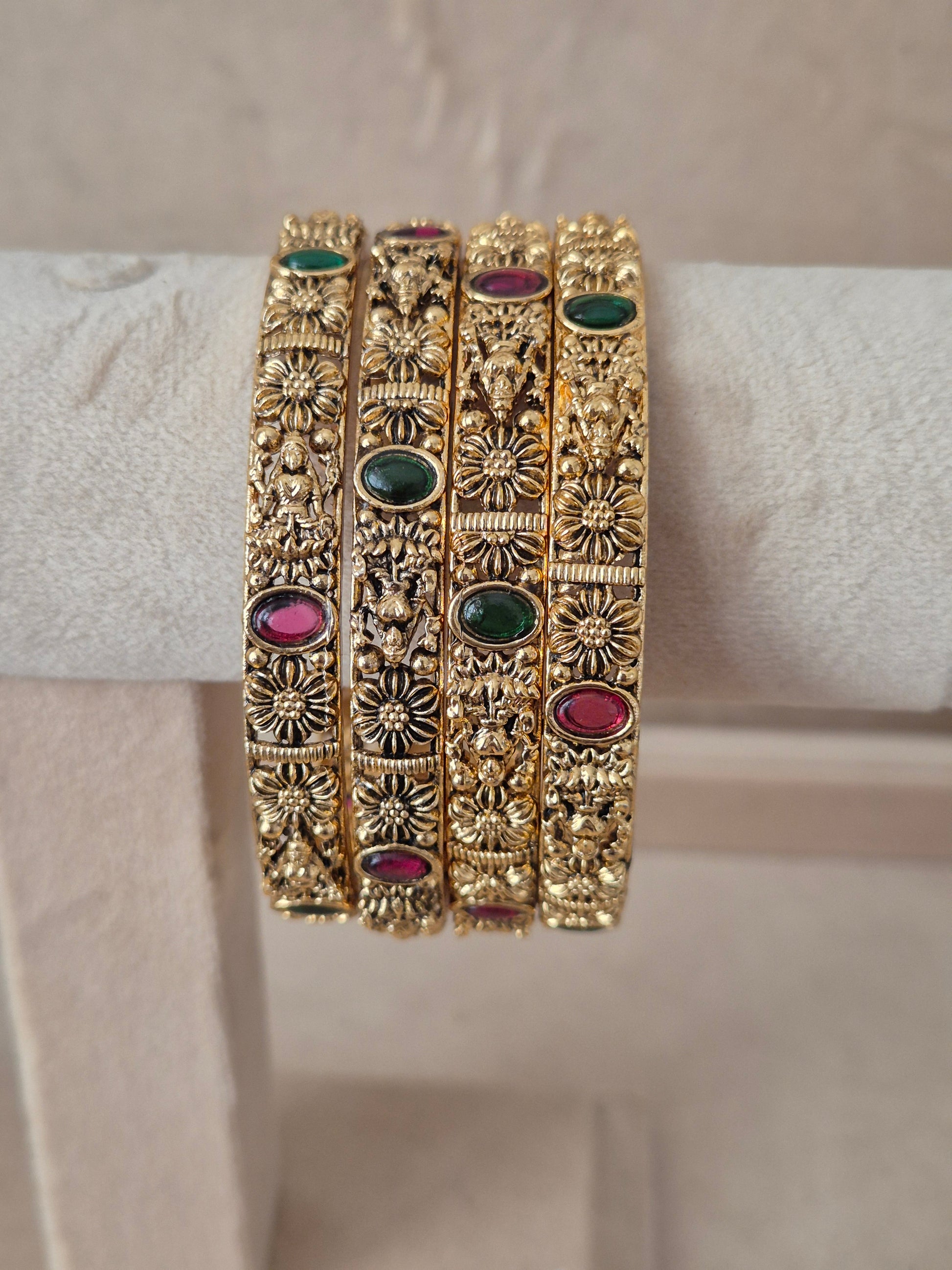 A set of four gold-plated Malvika bangles featuring intricate filigree metalwork inlaid with red and green gemstones, by naitri.in