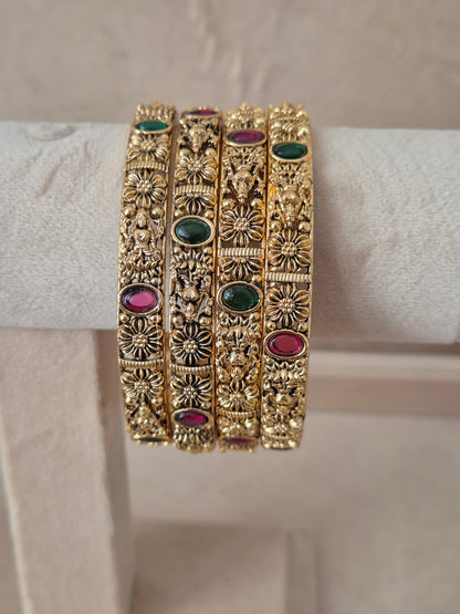 A set of four gold-plated Malvika bangles featuring intricate filigree metalwork inlaid with red and green gemstones, by naitri.in