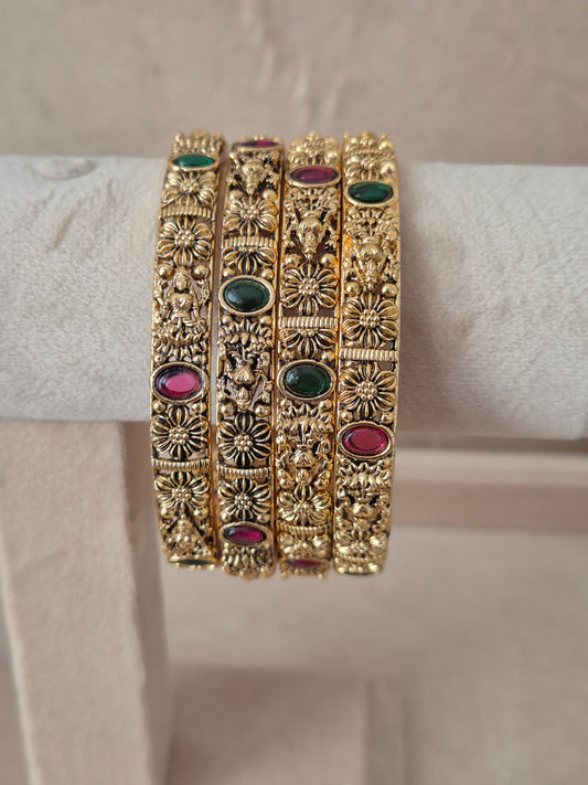 A set of four gold-plated Malvika bangles featuring intricate filigree metalwork inlaid with red and green gemstones, by naitri.in