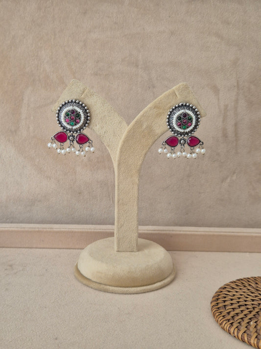 Pair of oxidized silver earrings with circular textured studs, pink stones, and small white pearl dangles by naitri.in