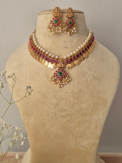 Handcrafted gold-plated chocker necklace featuring a white pearl collar, a row of square ruby-red stones, dangling gold coins, and a matching floral pendant set with matching drop earrings by najitri.in