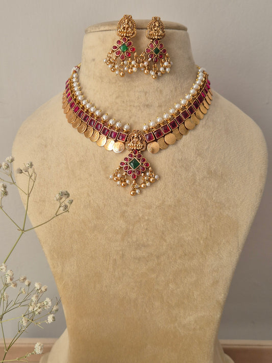 Handcrafted gold-plated chocker necklace featuring a white pearl collar, a row of square ruby-red stones, dangling gold coins, and a matching floral pendant set with matching drop earrings by najitri.in