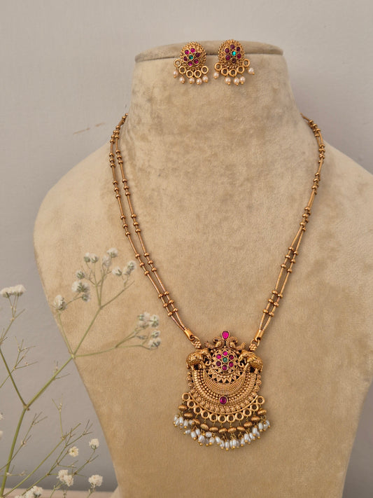 Handcrafted traditional gold-plated temple jewelry necklace featuring a delicate double-strand black and gold beaded chain, an intricate semicircular pendant with red and green stones, and dangling white pearl clusters with matching stud earring by naitri.in
