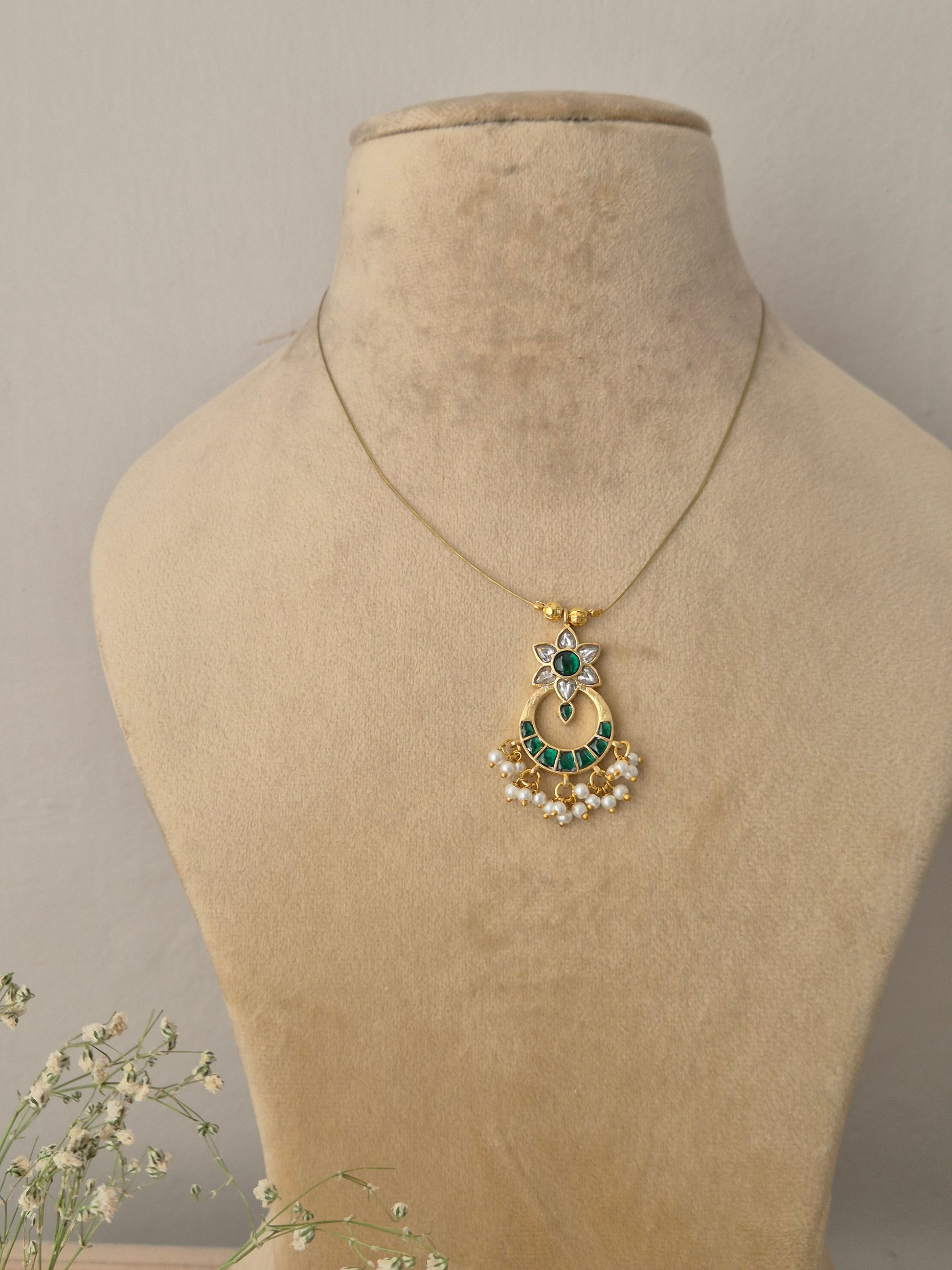 Handcrafted necklace featuring a gold-toned crescent moon pendant adorned with green stones, a central green emerald-like stone, and delicate white pearl droplets on a minimalist thin chain by naitri.in