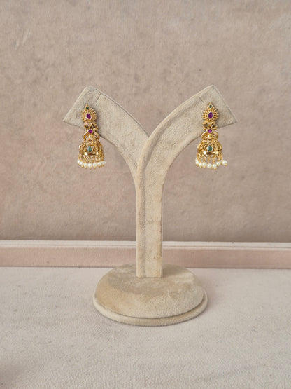 A pair of traditional Indian gold-toned jhumka earrings with colorful gemstone accents and white pearl bead borders, naitri.in