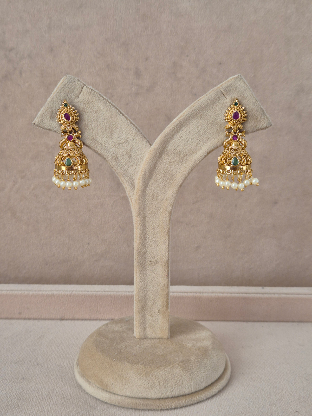A pair of ornate gold-toned Indian jhumka earrings with red and green stones and white pearl fringe, by naitri.in