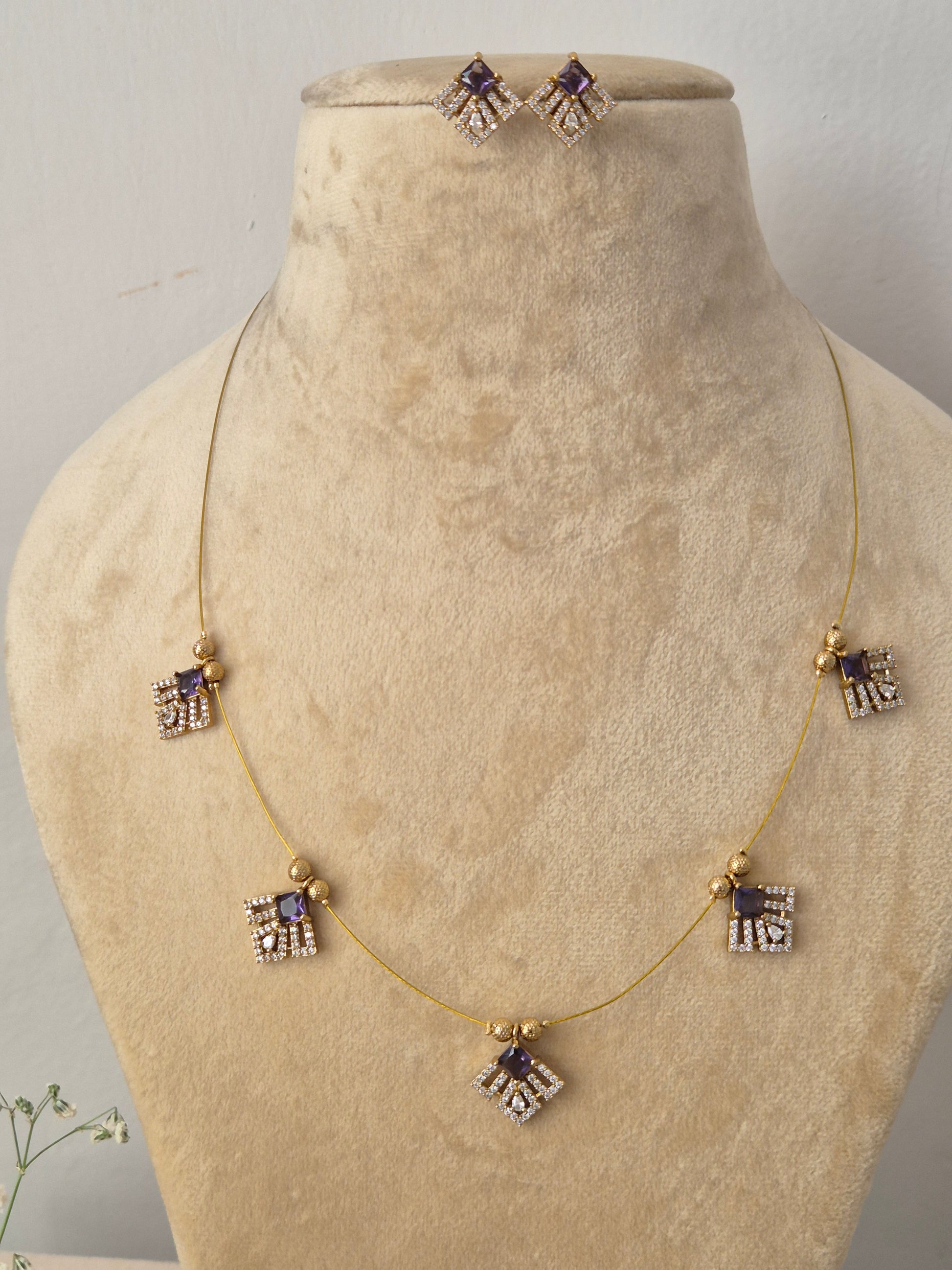 Modern Indian style gold chain necklace set with purple stone embellishments. Handcrafted delicate gold pendant necklace and earring set showcasing geometric crystal charms by naitri.in