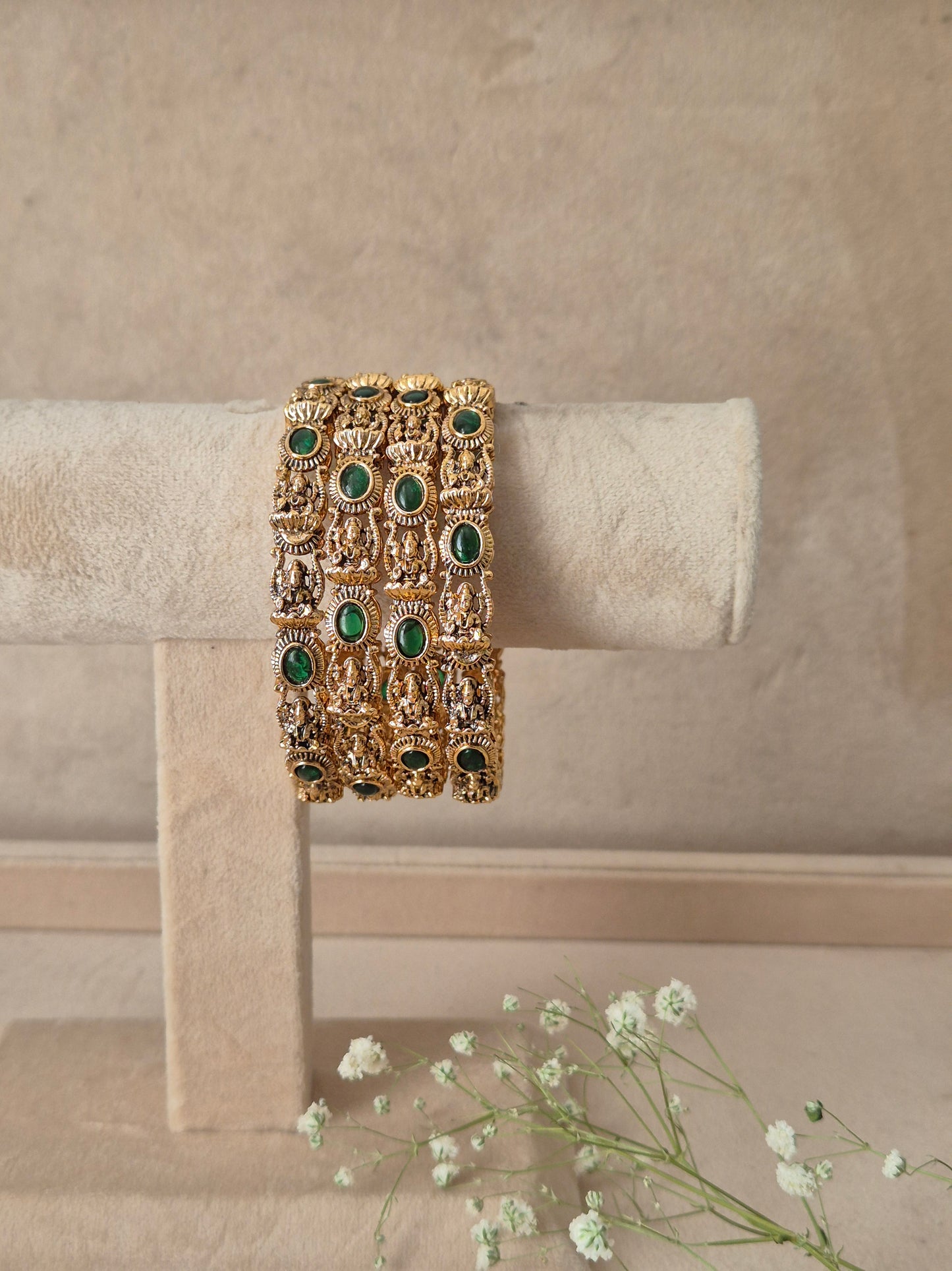 Set of 4 traditional gold-plated antique bangles decorated with oval-cut emerald green gemstones and intricate floral carvings, by naitri.in