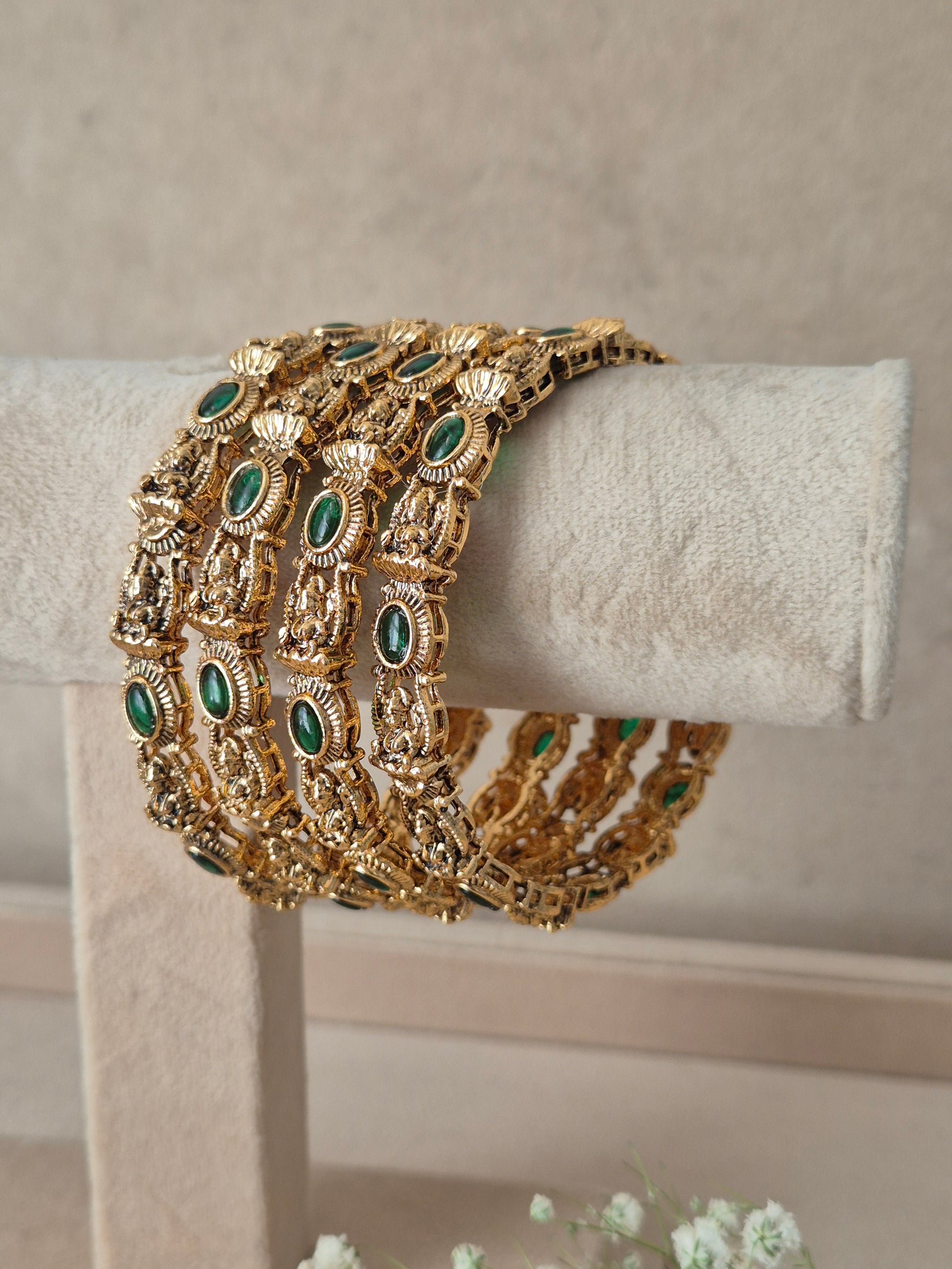 Traditional Indian gold-plated antique bangles adorned with oval green gemstone accents, Antique gold-plated bangle set decorated with green gemstones by naitri.in