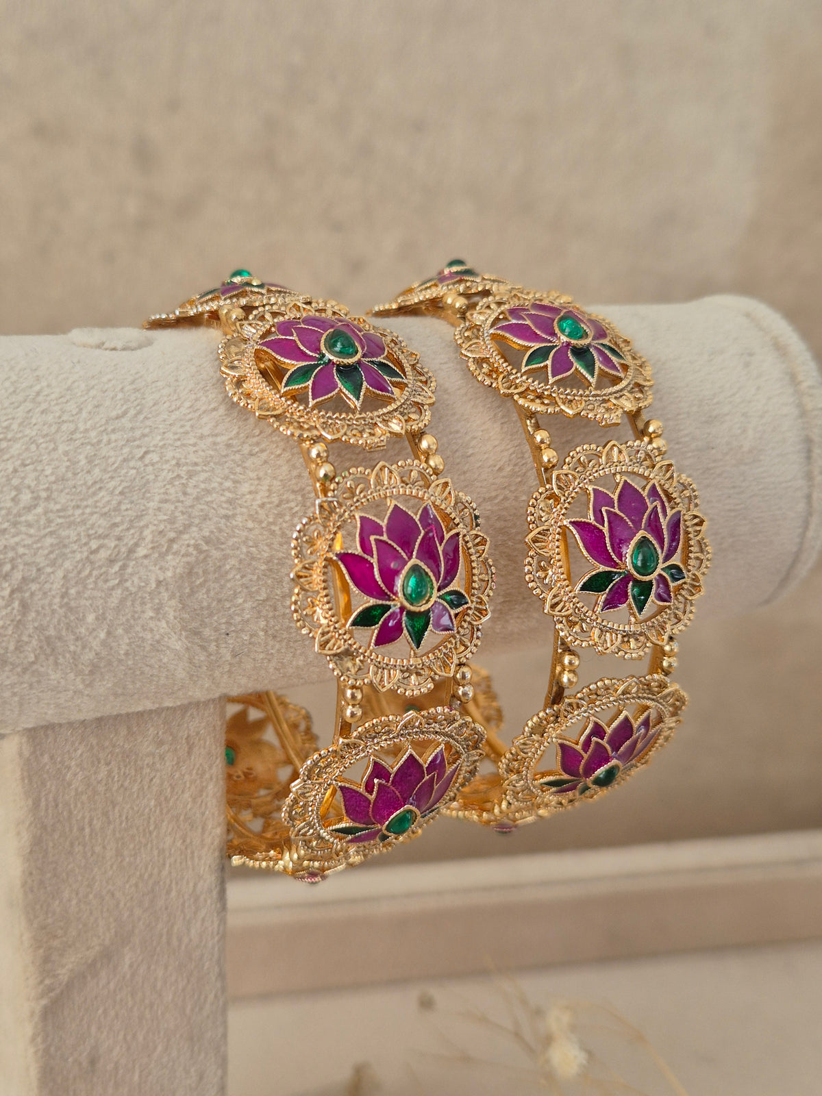 Festive Indian gold-plated bangles adorned with vibrant pink lotus artwork and emerald-colored stone highlights for weddings and special occasions by naitri.in