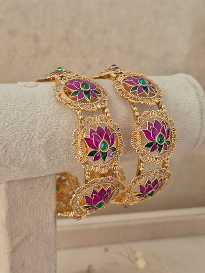 Festive Indian gold-plated bangles adorned with vibrant pink lotus artwork and emerald-colored stone highlights for weddings and special occasions by naitri.in
