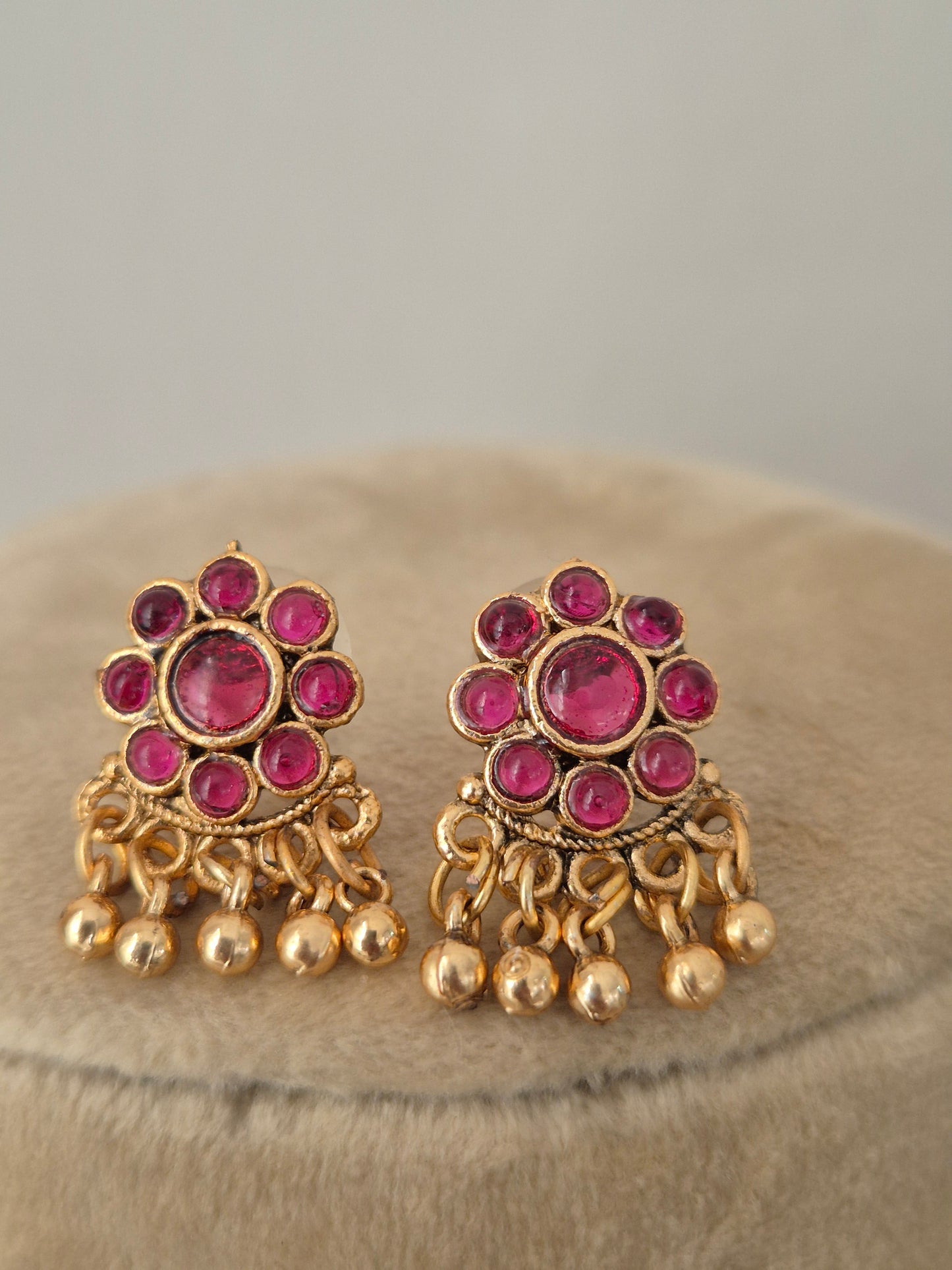 Antique gold-toned earrings intricate metallic round floral vibrant red stone clusters, and delicate hanging gold bead drops by naitri.in