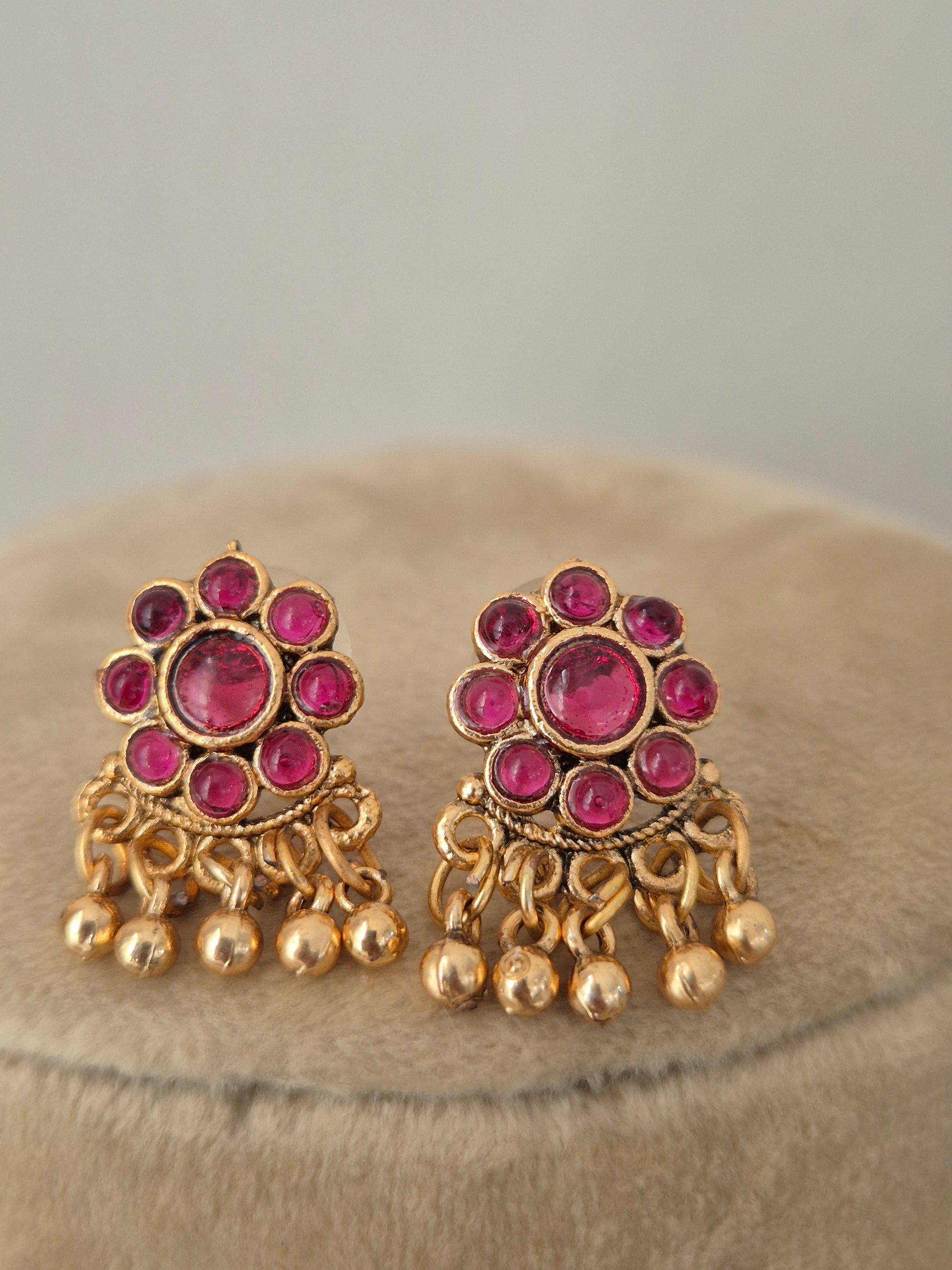 Antique gold-toned earrings intricate metallic round floral vibrant red stone clusters, and delicate hanging gold bead drops by naitri.in