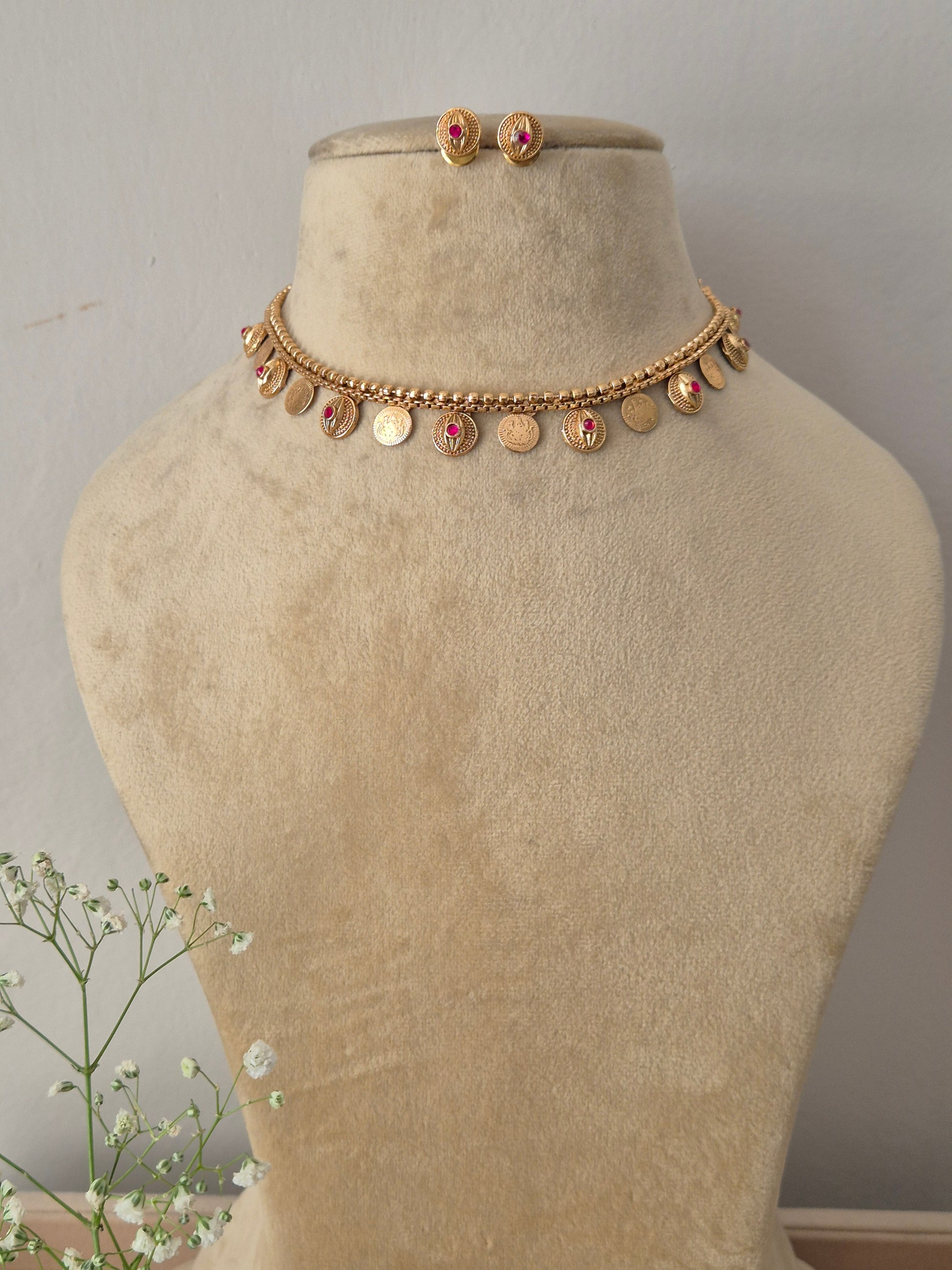 Gold choker necklace with hanging coin-shaped charms and a pink gemstone center, with matching stud earrings by naitri.in  
