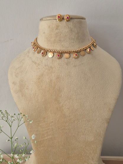 Gold choker necklace with hanging coin-shaped charms and a pink gemstone center, with matching stud earrings by naitri.in  