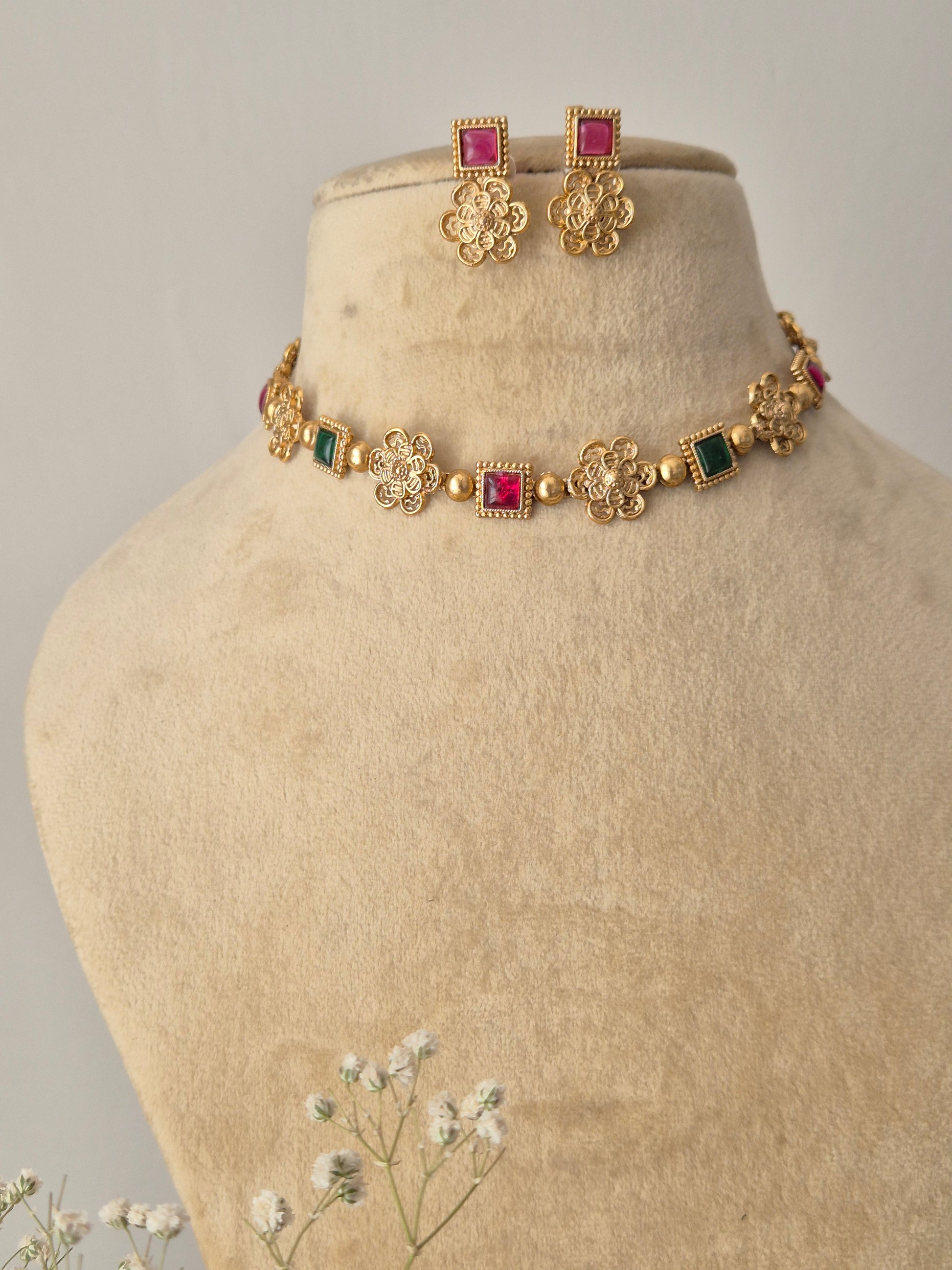 Mihika floral stone choker set: A gold-finish brass necklace with vibrant red and green stones and coordinating pink earrings by naitri.in