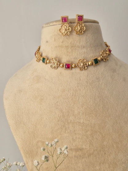 Mihika floral stone choker set: A gold-finish brass necklace with vibrant red and green stones and coordinating pink earrings by naitri.in
