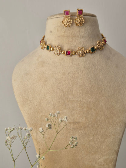 Handcrafted gold-plated brass choker with floral metalwork motifs, alternating square red and green stones, and matching pink stud earrings by naitri.in