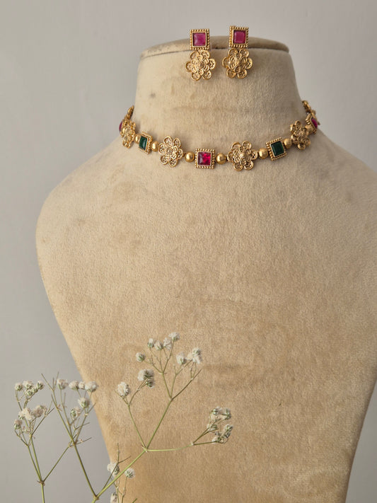 Handcrafted gold-plated brass choker with floral metalwork motifs, alternating square red and green stones, and matching pink stud earrings by naitri.in