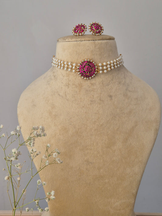 Choker Set featuring a multi-strand white pearl choker with a central pink stone floral pendant and matching pink stud earrings by naitri.in