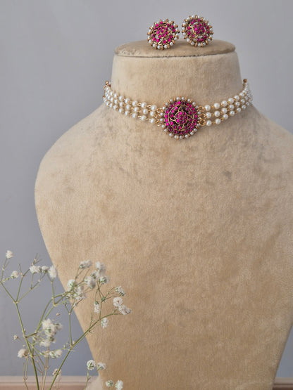 traditional Indian-style pearl choker with a ruby-pink stone floral medallion, displayed on a beige bust with delicate baby's breath flowers by naitri.in