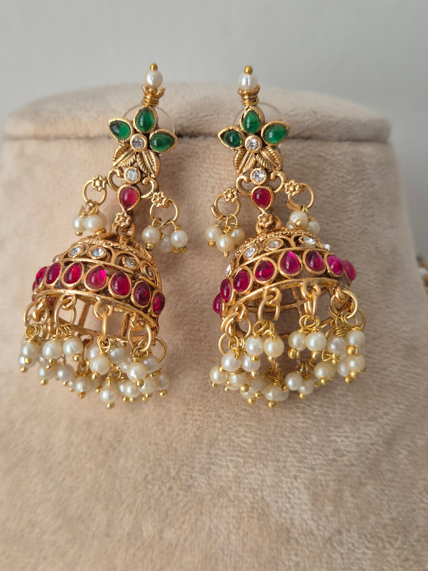 A pair of gold-plated Indian jhumka earrings decorated with white pearls, green emerald-cut stones, and pink ruby-cut stones, by naitri.in