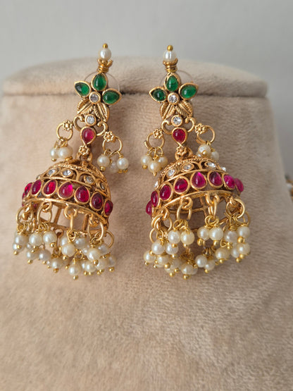 A pair of gold-plated Indian jhumka earrings decorated with white pearls, green emerald-cut stones, and pink ruby-cut stones, by naitri.in
