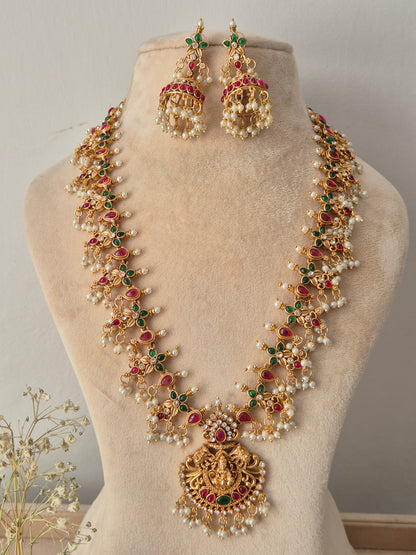Gold-plated traditional Indian long necklace and earring set featuring red and green stone accents, pearl clusters, and an ornate deity pendant by naitri.in