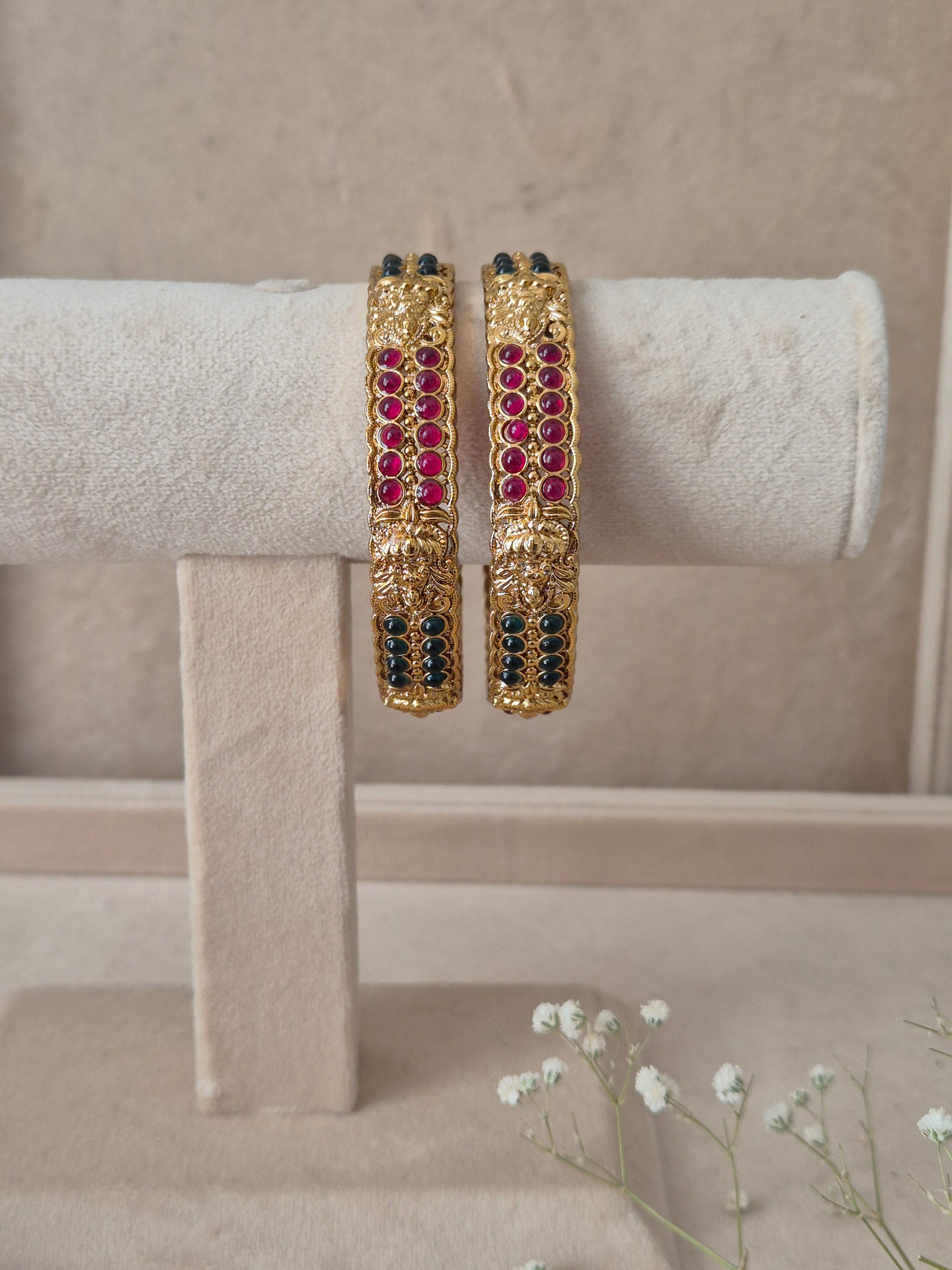 Set of 2 Mitanshi gold bangles by Naitri featuring intricate traditional patterned engravings, accented with rows of ruby-red and dark green gemstone by naitri.in