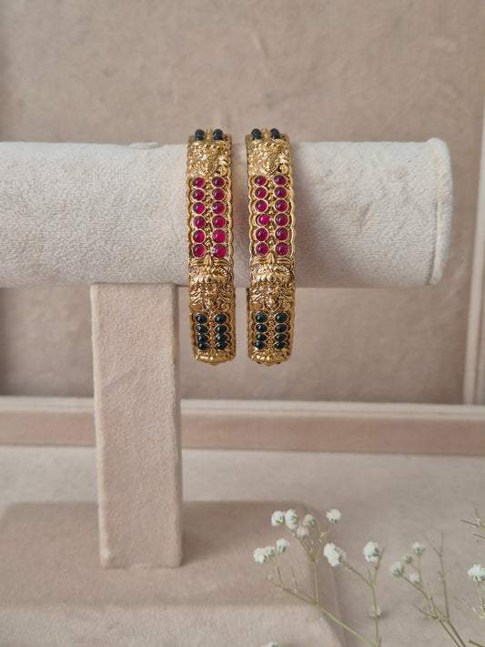 Set of 2 Mitanshi gold bangles by Naitri featuring intricate traditional patterned engravings, accented with rows of ruby-red and dark green gemstone by naitri.in