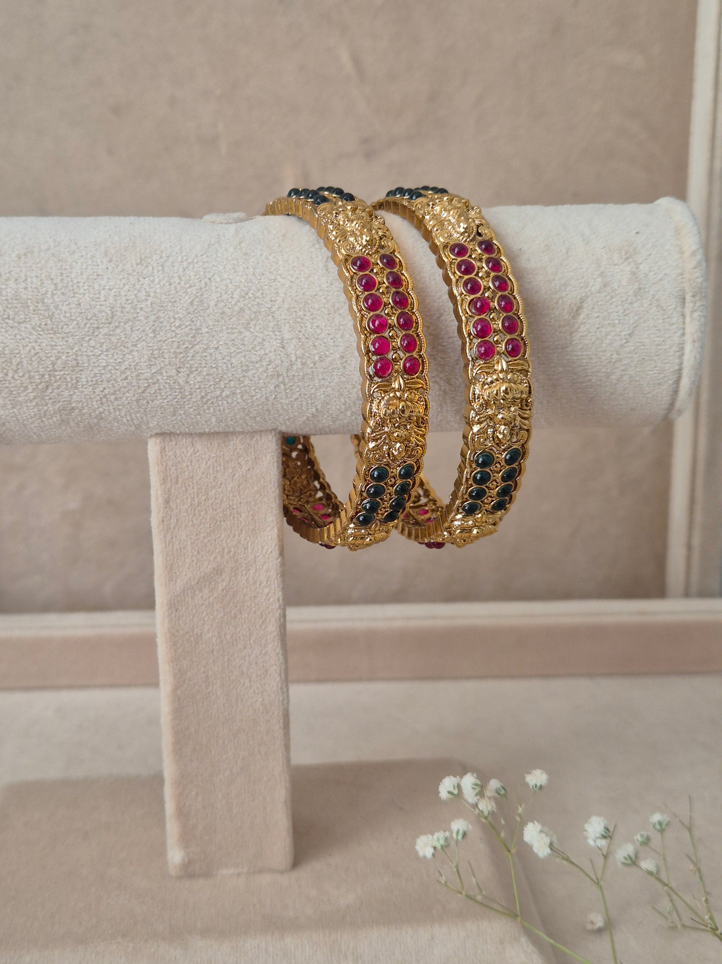 Two traditional gold-plated ethnic bangles with detailed geometric patterns and inlaid red and green gemstones by naitri.in