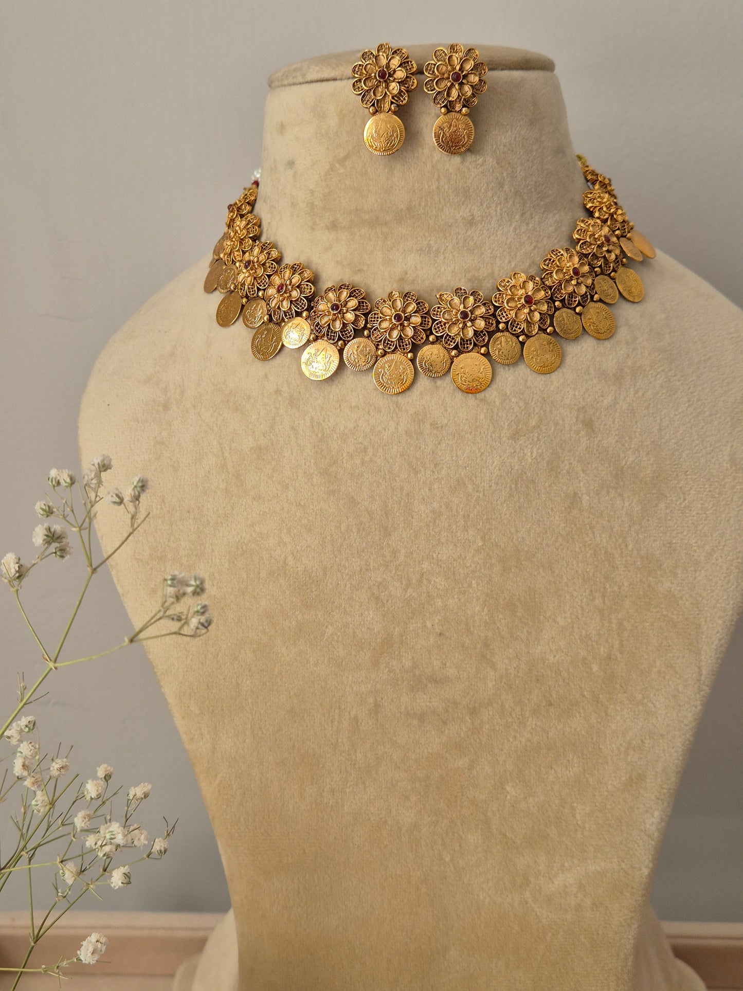Handcrafted gold-polished brass choker necklace featuring intricate floral metalwork and a dangling coin fringe, with matching round floral stud earrings by naitri.in