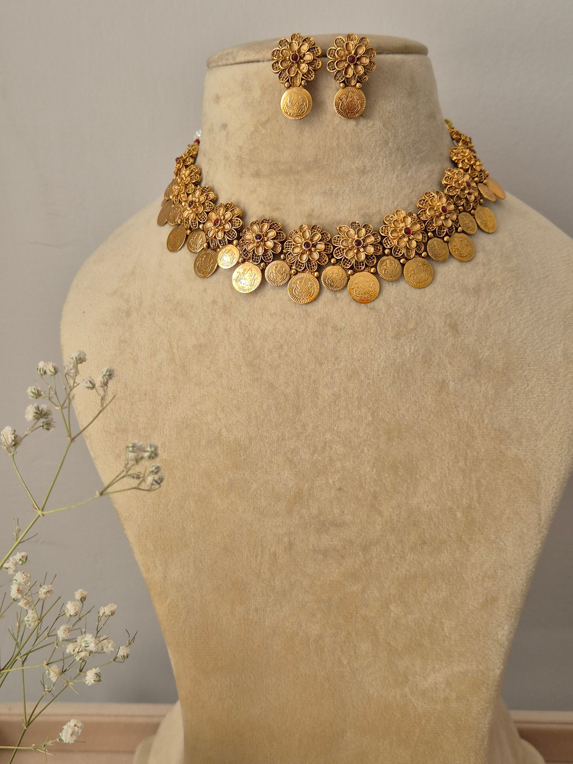 Handcrafted gold-polished brass choker necklace featuring intricate floral metalwork and a dangling coin fringe, with matching round floral stud earrings by naitri.in