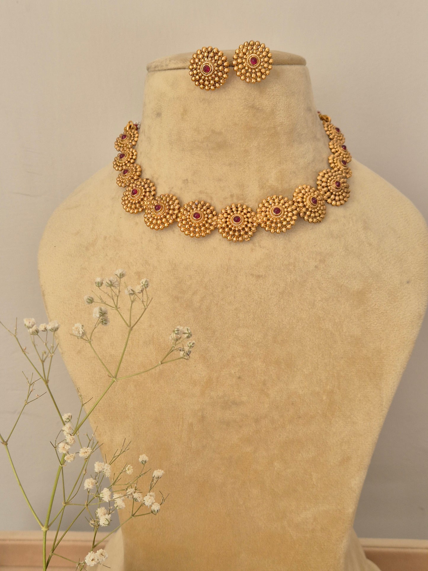 Handcrafted gold-plated temple jewelry choker featuring a row of circular floral wheel motifs with ruby-red stone centers and matching round stud earrings by naitri.in
