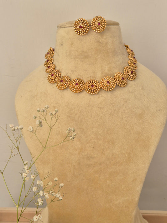 Handcrafted gold-plated temple jewelry choker featuring a row of circular floral wheel motifs with ruby-red stone centers and matching round stud earrings by naitri.in