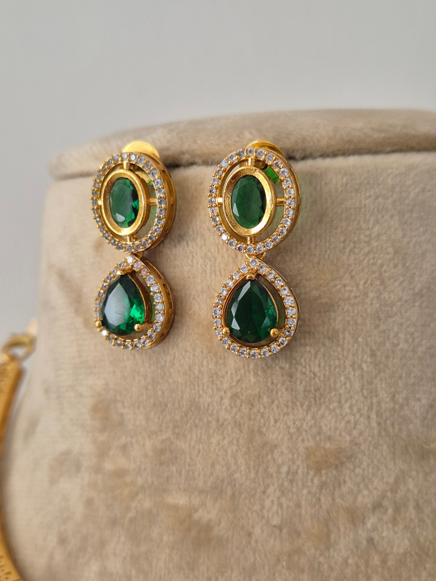 Gold-plated ethnic earrings featuring a prominent oval-cut green stone pendant surrounded by crystals teardrop earrings by naitri.in